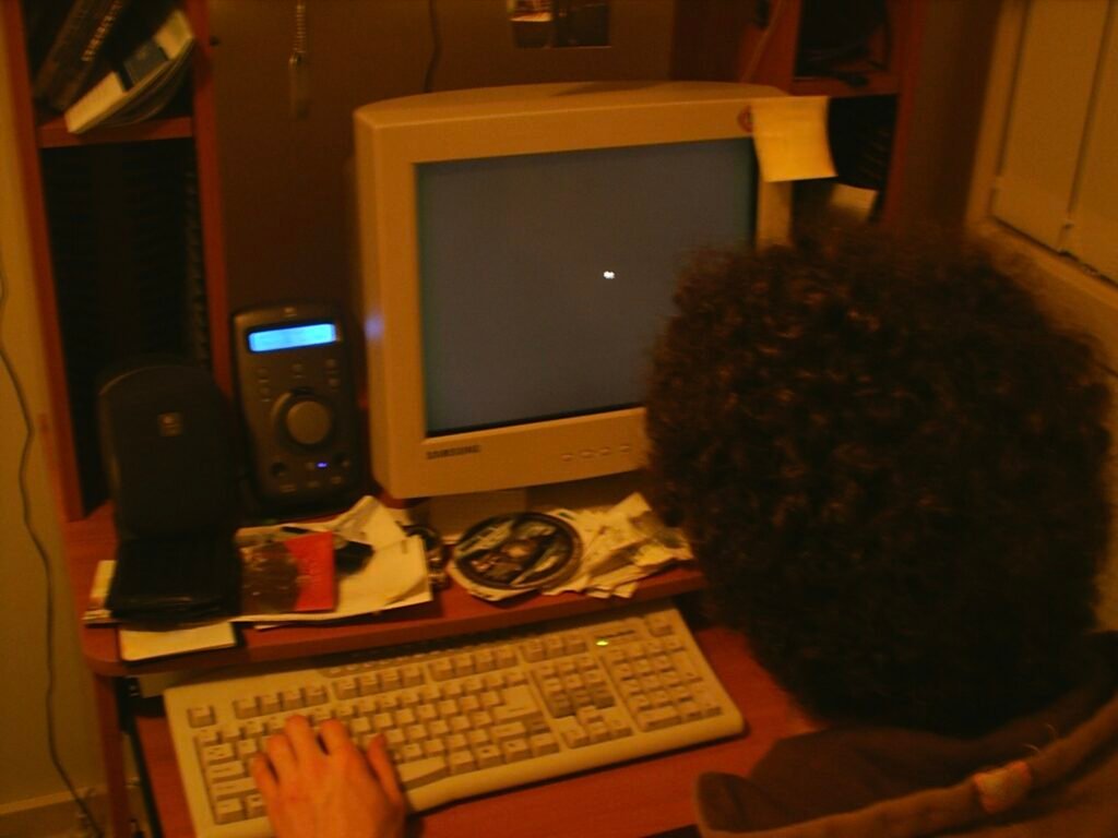 Old photo of me sitting at my early‑2000s computer setup with a CRT monitor and beige keyboard, facing away from the camera. The screen is blank, capturing the nostalgic look of my desk during the Blaster worm era.